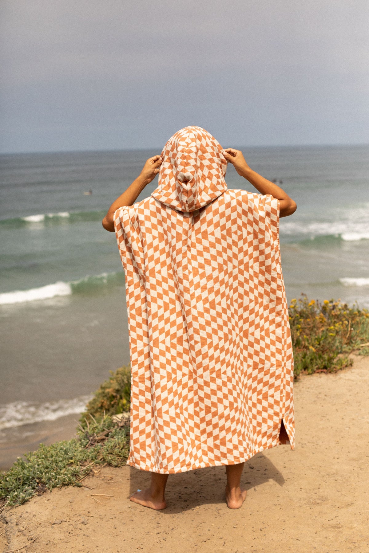 Back view of the Terracotta Pro Eco Poncho with the hood up, looking at the ocean - Leus Towels Australia