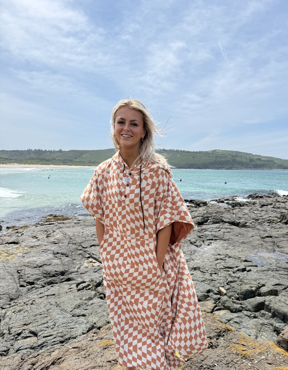 Woman wearing the Terracotta Pro Eco Poncho on the rocks at the beach - Leus Towels Australia