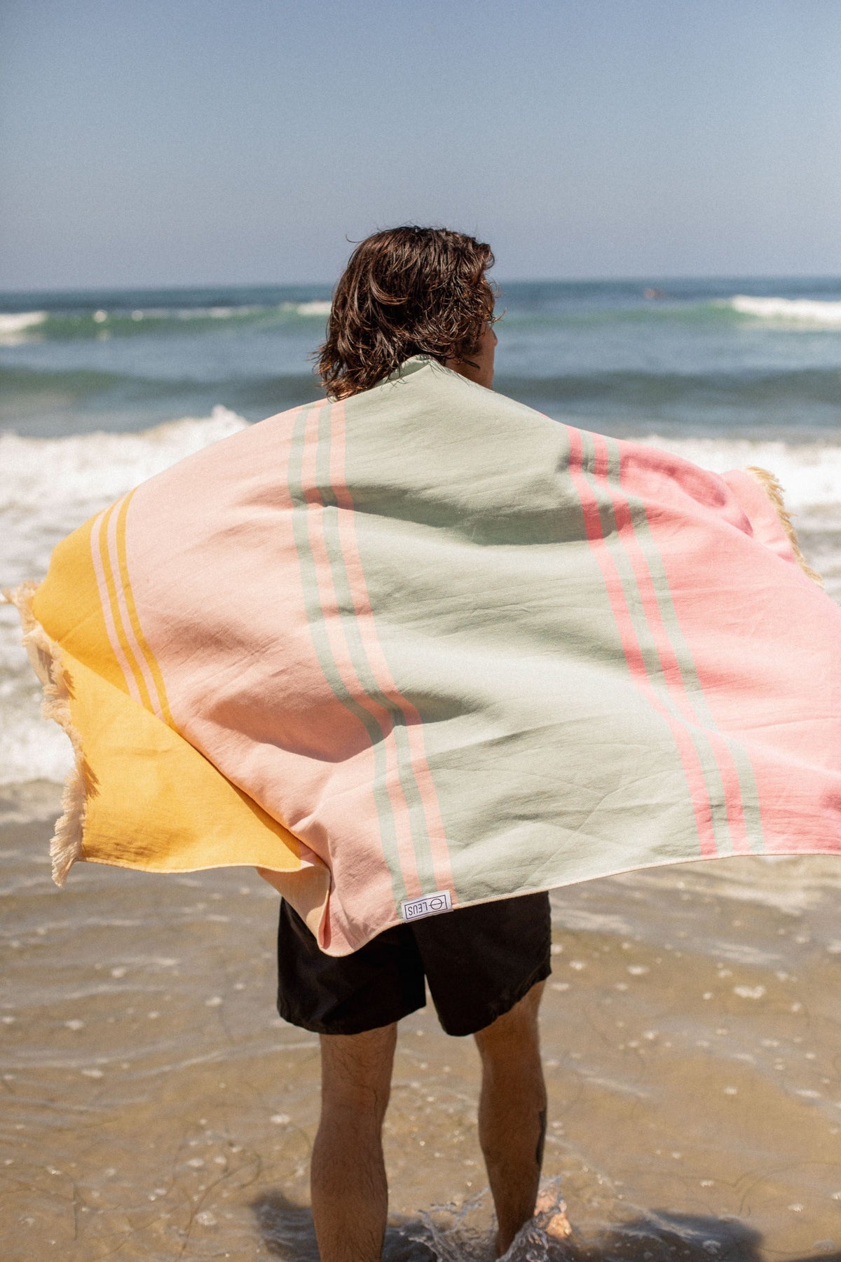 Zuma Turkish Eco Towel: man holding it in the wind at the beach - Leus Towels Australia