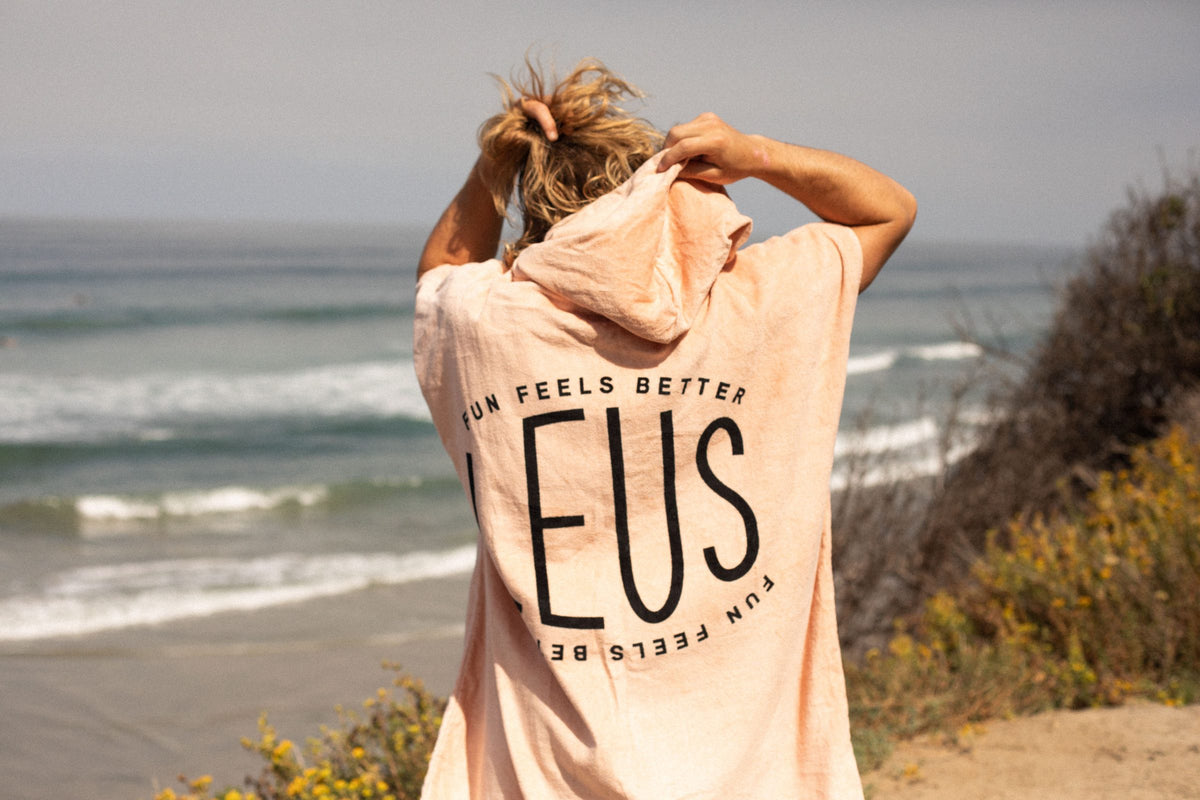 LEUS hooded eco poncho with the Fun Feels Better back print, overlooking the ocean